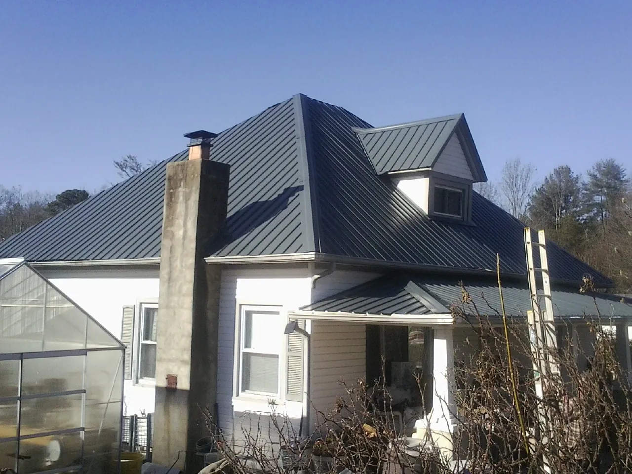 Dark blue standing seam metal roof on a white farmhouse with dormer — Slate & Tile Roof Repair by Roofing Brothers in Irmo