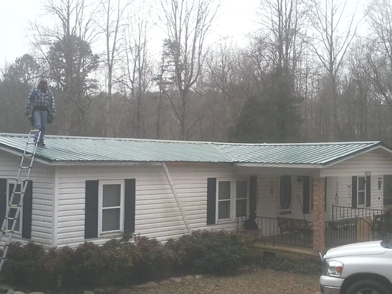 Worker on a ladder beside a new green metal roof on a ranch home in Irmo
