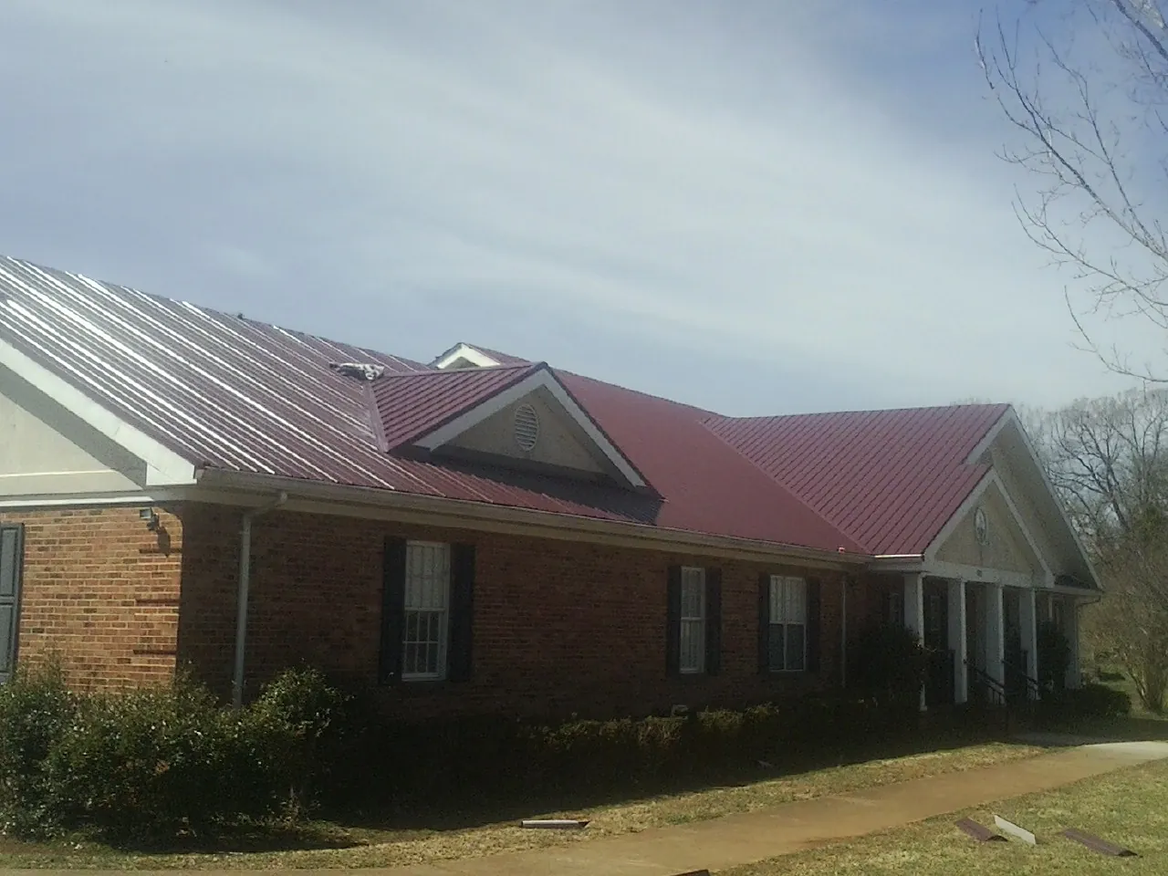 Red metal roof with gabled entries on a long brick building, from a Hail Damage Roof Repair job in Irmo