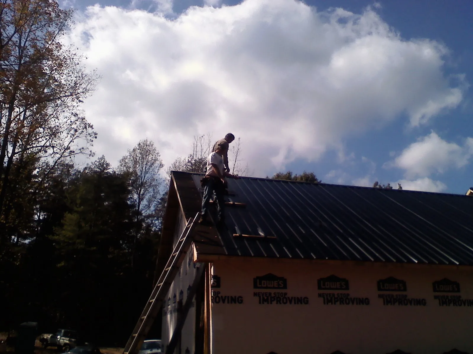 Roofer fastening dark metal panels high against a cloudy sky, from a Roof Inspection job in Irmo