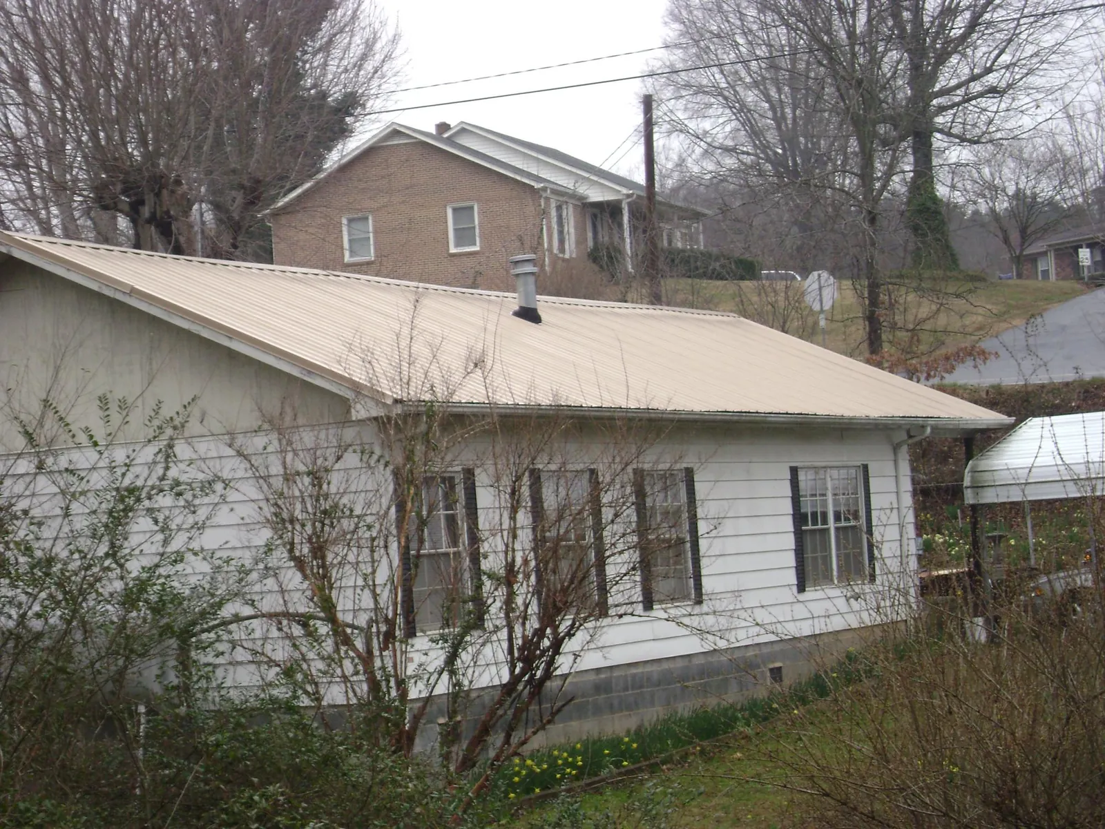 Tan metal roof on a white sided house set into a hillside — Commercial Roofing by Roofing Brothers in Irmo